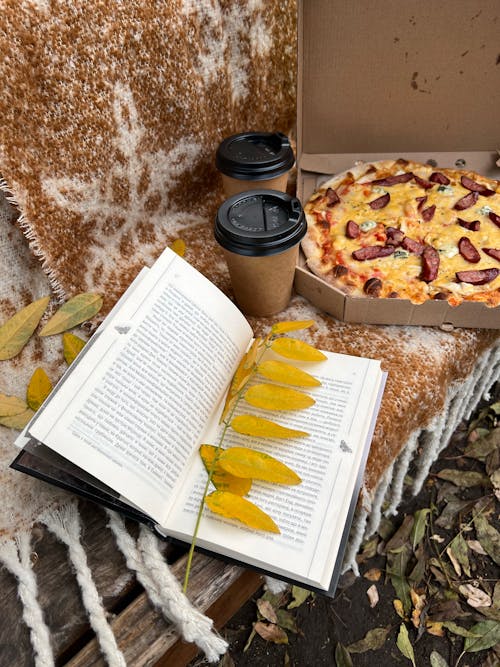 An Open Book with Leaves Near the Box of Pizza and Coffee
