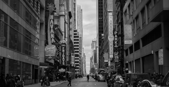 Black and white cityscape of a busy urban street in New York City with skyscrapers and signs.
