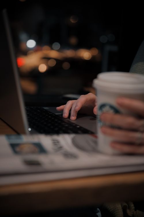 Free A person using a laptop in a dimly lit coffee shop, enjoying a warm drink. Stock Photo