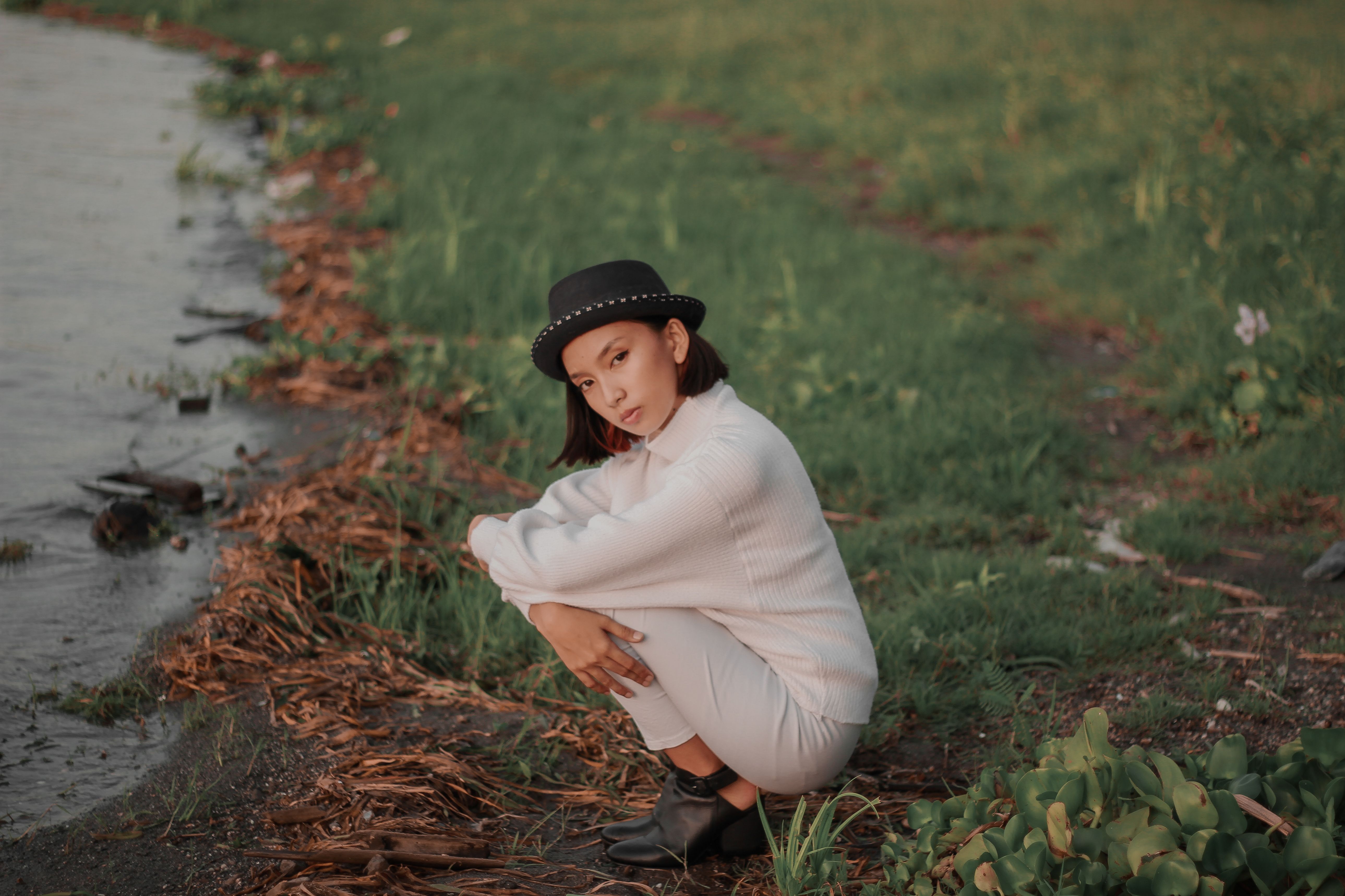 A Woman in White Knitted Sweater Sitting on Grass Field while Looking ...