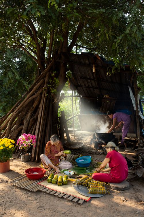 Free Women preparing traditional food outdoors by a rustic hut, under a large tree. Stock Photo