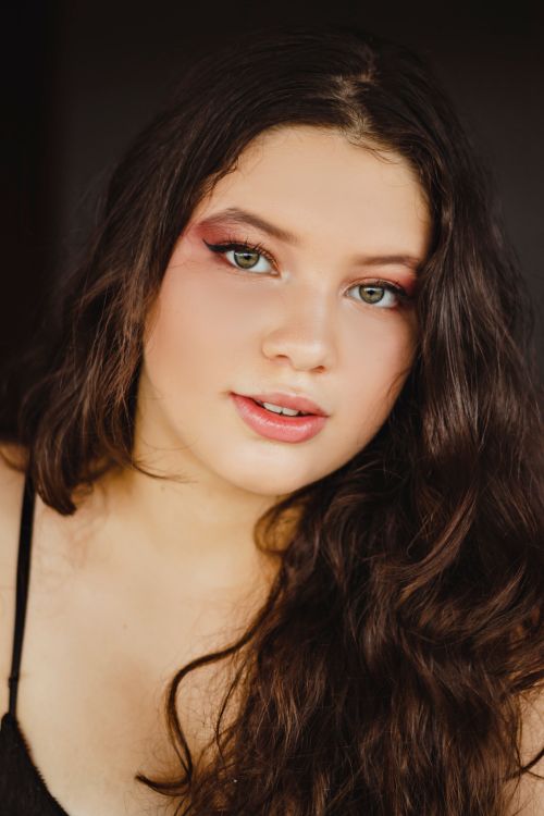 Free Stunning portrait of a young woman with wavy brown hair, makeup, and soft lighting. Stock Photo