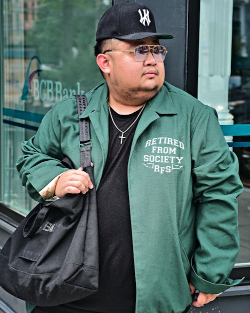 A Man in Green Jacket Wearing Sunglasses while Carrying His Bag