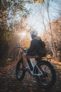 Man on a bicycle riding through a sunlit autumn forest path.