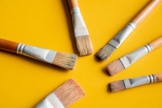 Flat lay of paintbrushes in a circular arrangement on a yellow surface, perfect for art themes.