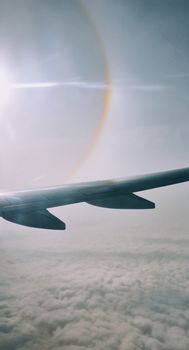 View from an airplane window featuring a sun halo and clouds, captured mid-flight.