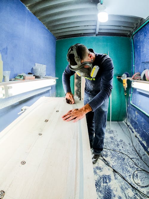 Carpenter in Face Mask Planing Wood in Small Workshop