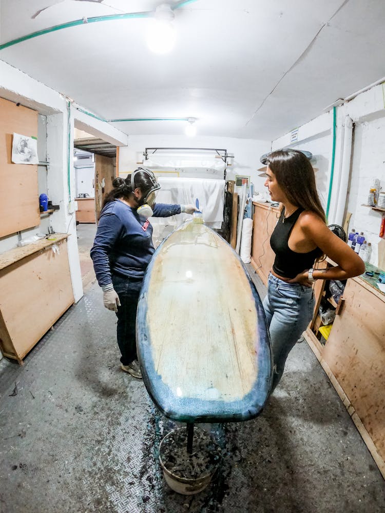 Worker Painting Surfboard In Workshop