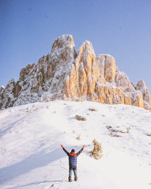 A Back View of a Person Standing on a Snow Covered Ground Near the Rocky Mountain while Raising Hands