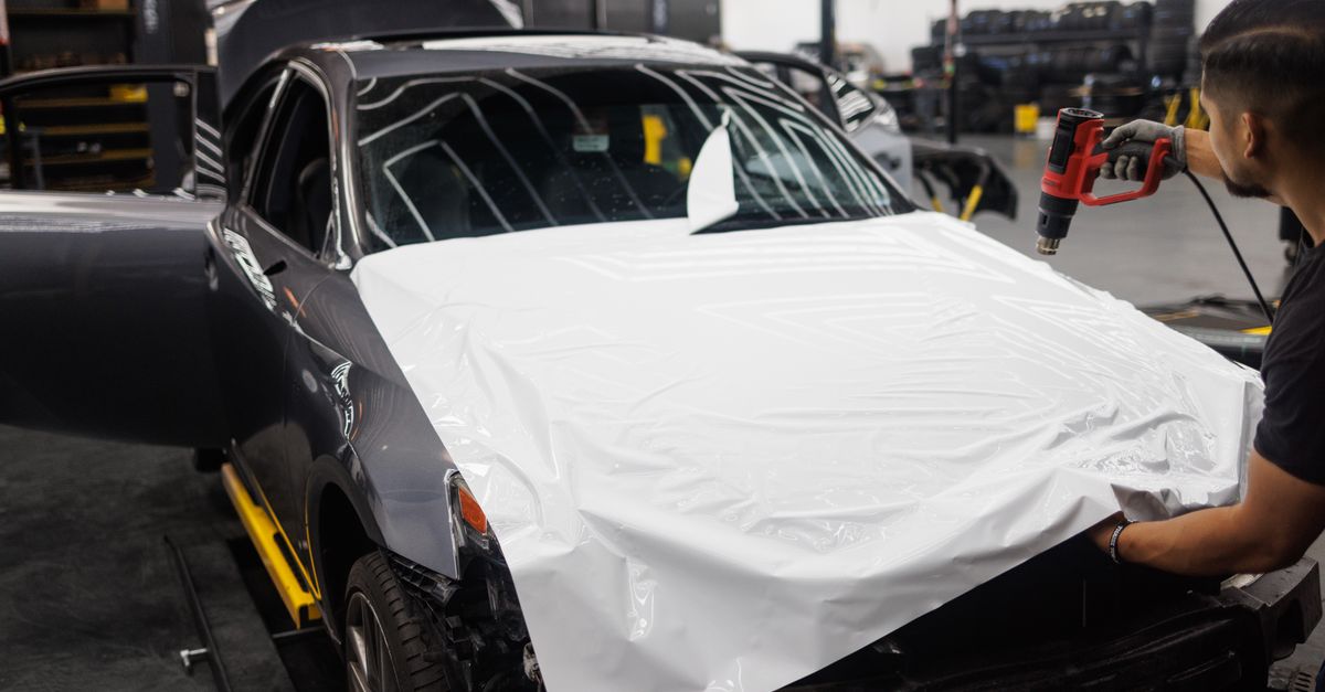 Car being wrapped with white vinyl in an auto workshop by a skilled mechanic.