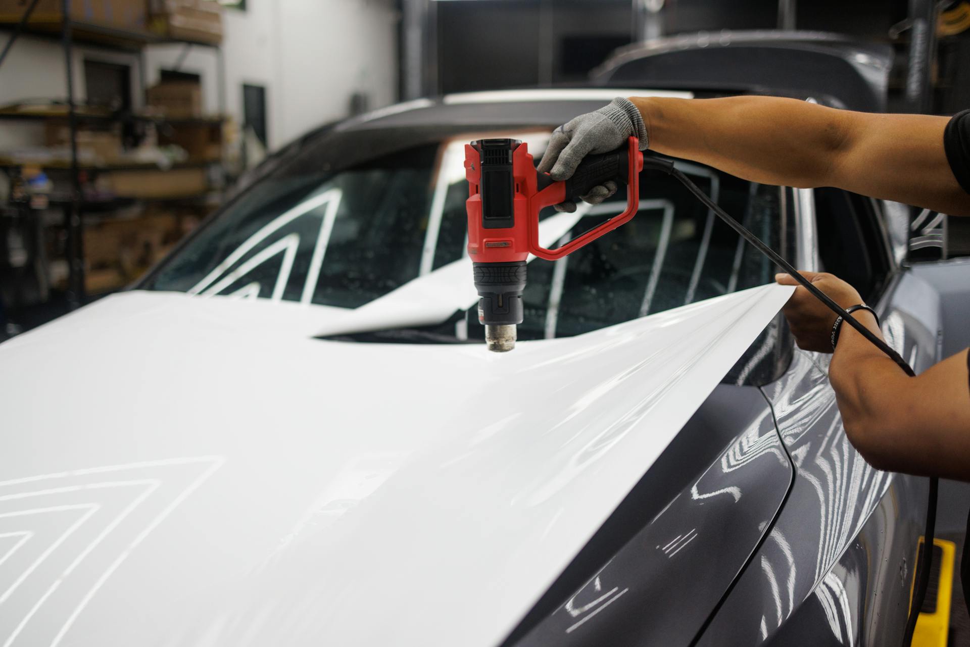 Worker applying a car wrap using a heat gun for precise adhesion.