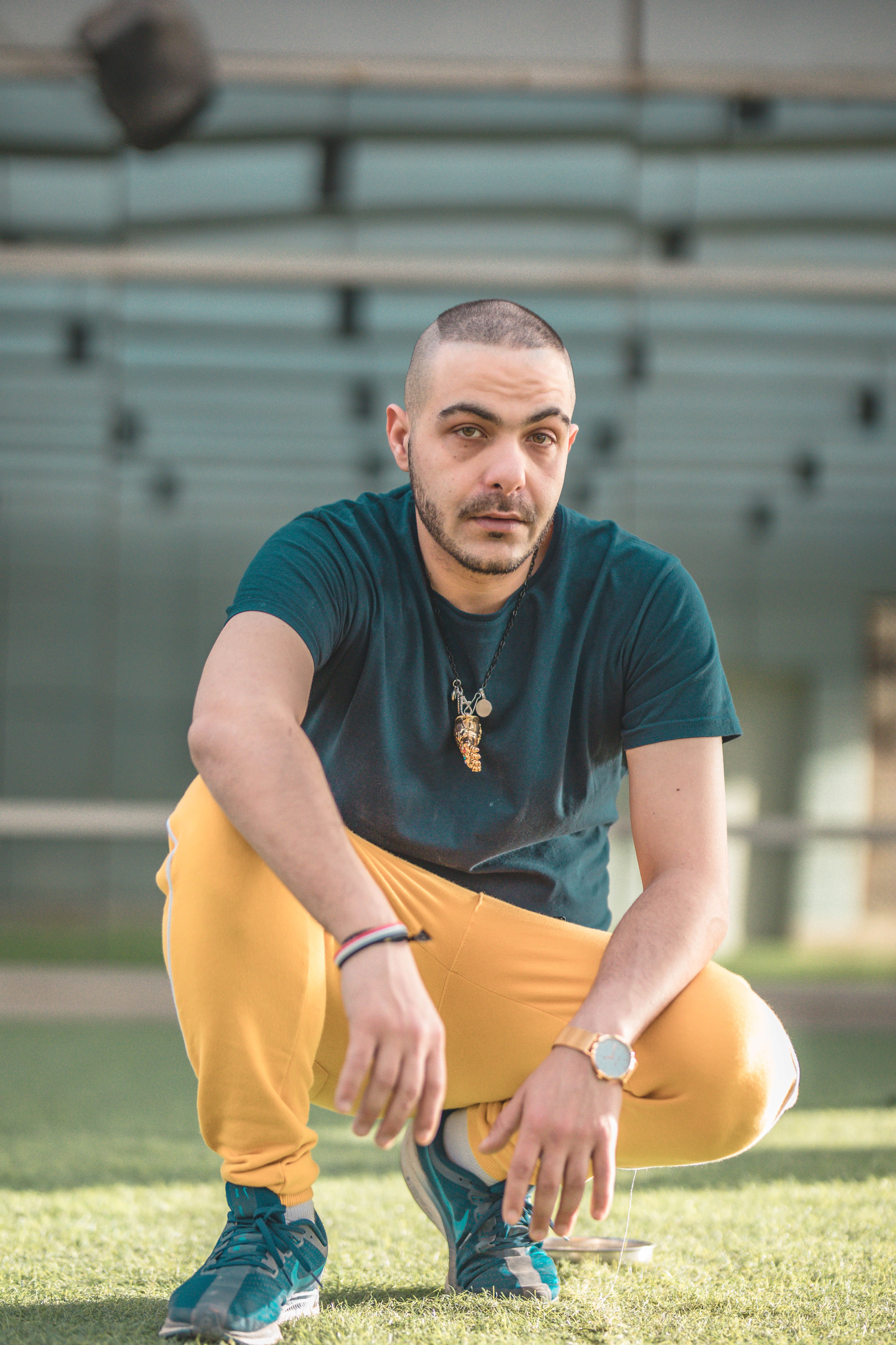 Stylish man squatting outdoors in vibrant clothing, showcasing modern fashion sense.