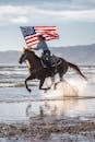 骑马的妇女在海边疾驰，在阳光明媚的格罗弗海滩上挥舞着美国国旗