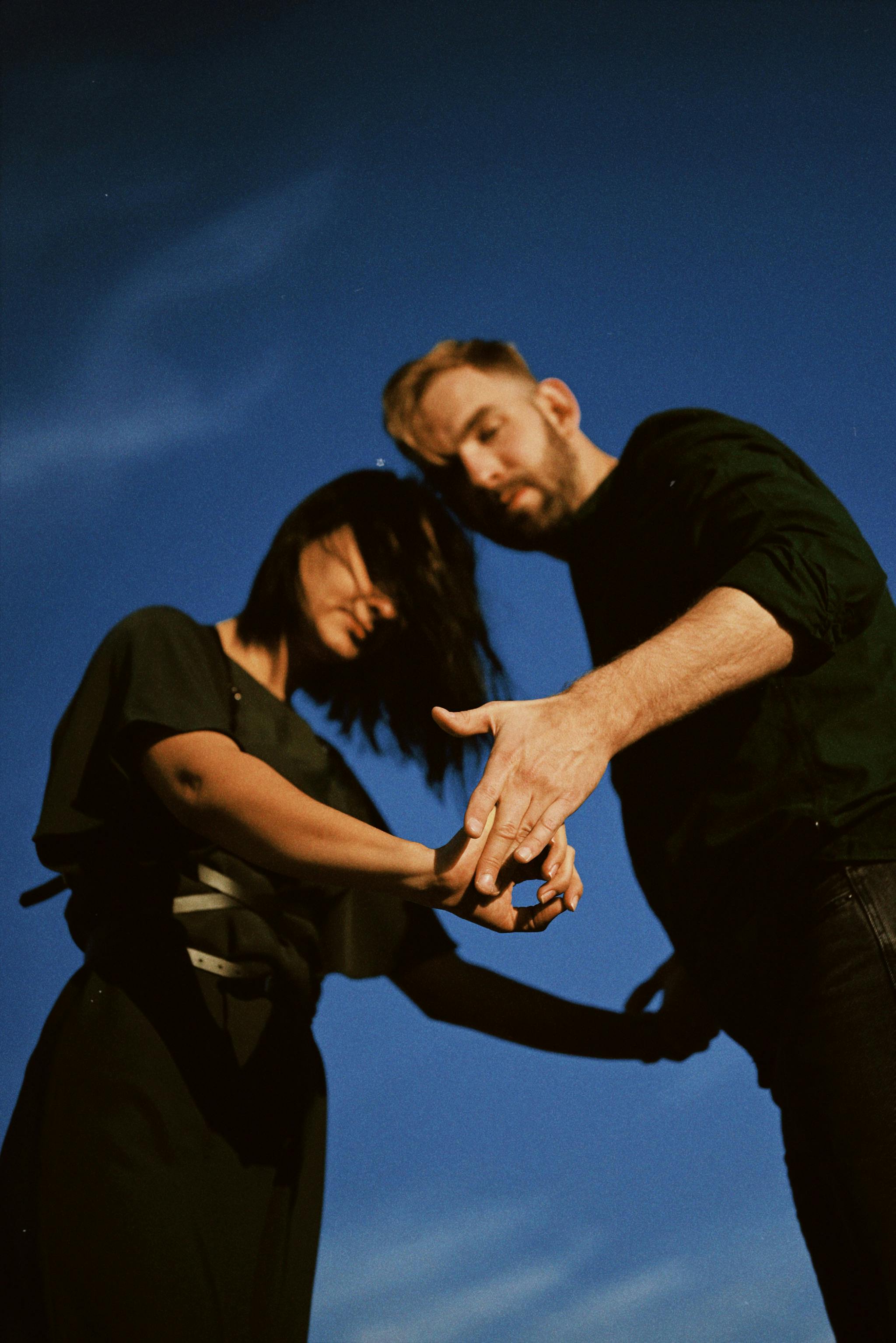 A couple holding hands outdoors under a clear blue sky, low-angle shot capturing intimacy and connection.