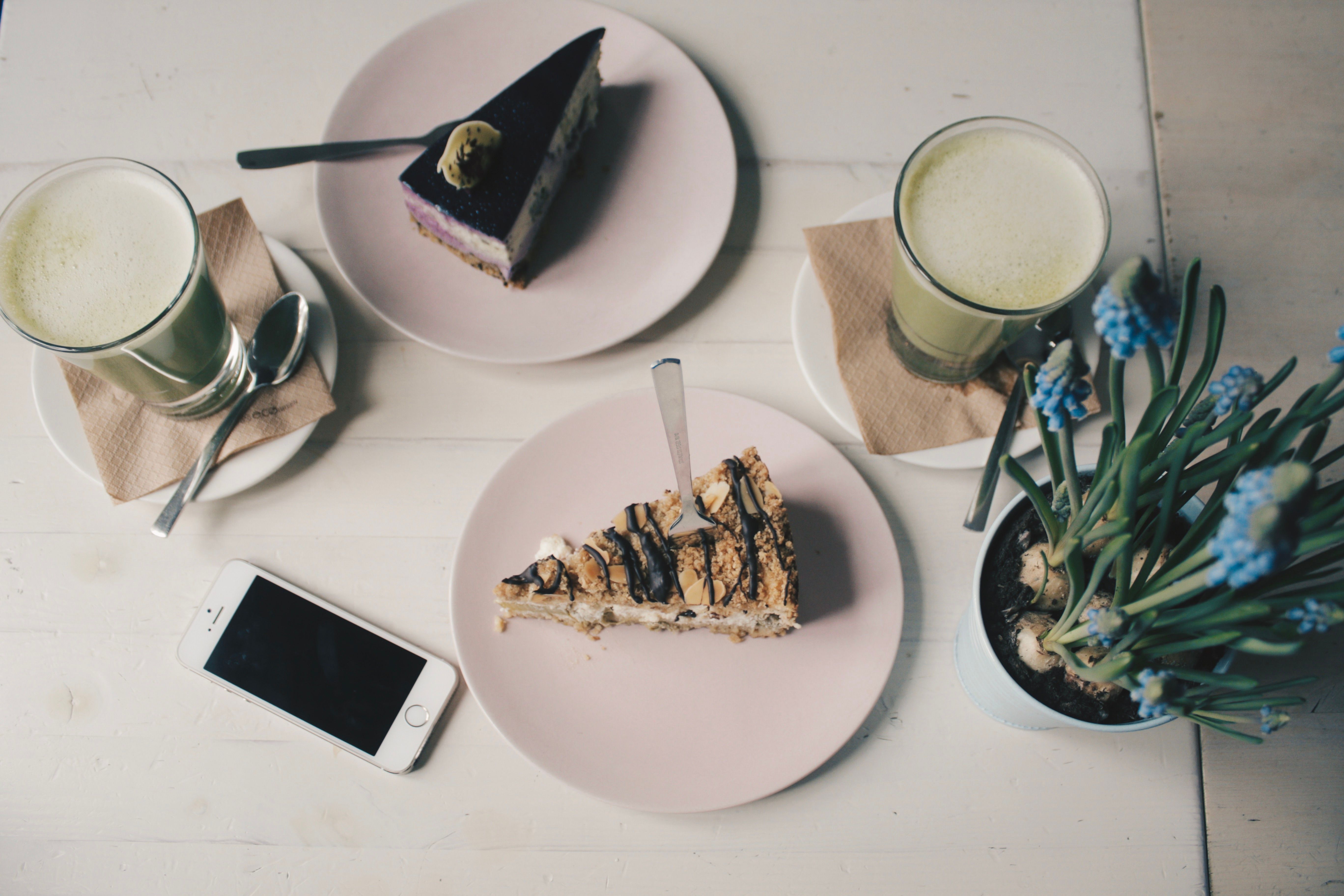 Chic dessert table with cakes, green tea lattes, smartphone, and flowers - perfect for modern cafes and food photography.