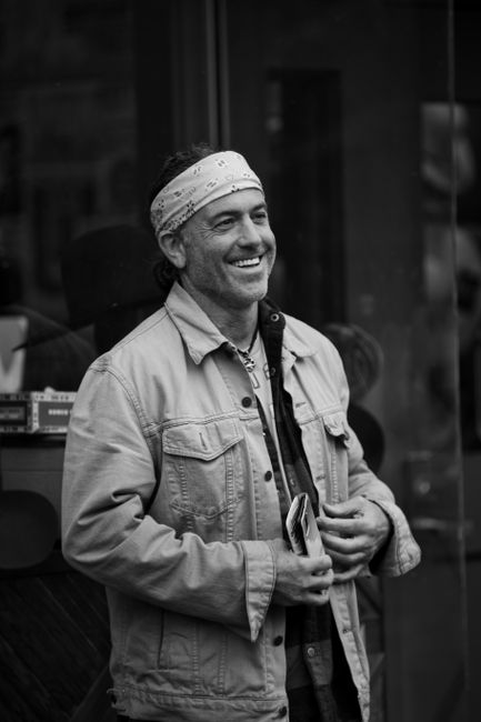 Black-and-white portrait of a man smiling in a denim jacket, Nashville street scene.