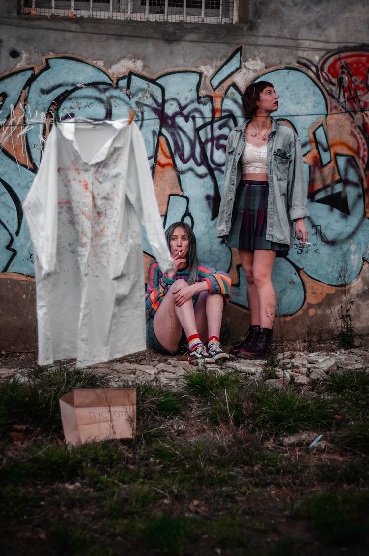 Women Smoking Cigarettes Under Graffitied Wall