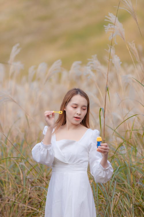 Woman in White Dress Playing with Soap Bubbles in the Field