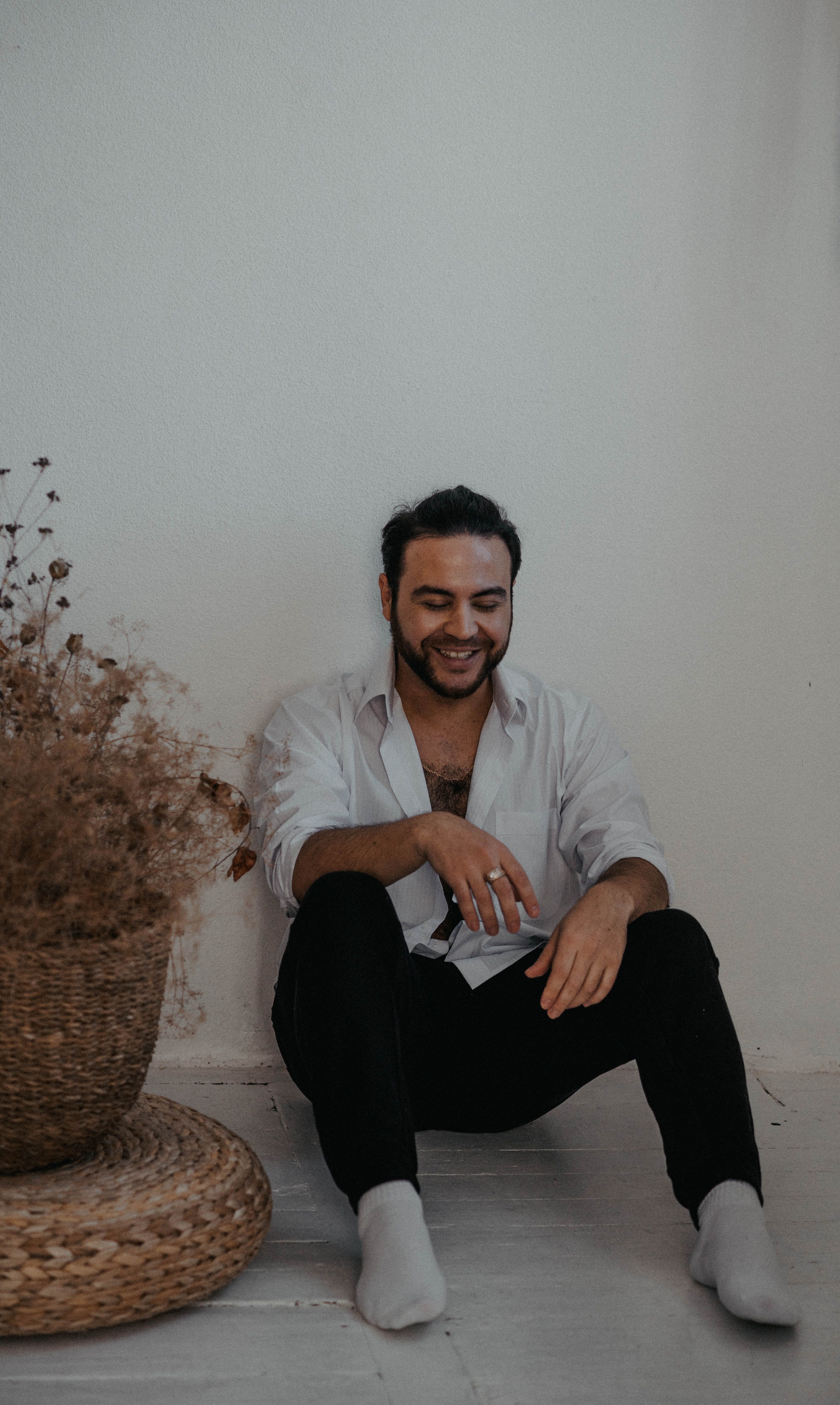 Smiling man sitting against a wall with a basket of dried flowers, capturing a cozy and warm moment.