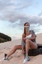 Young Woman in Art Makeup Sitting on Tire on Sandy Beach