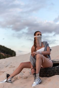 Young Woman in Art Makeup Sitting on Tire on Sandy Beach