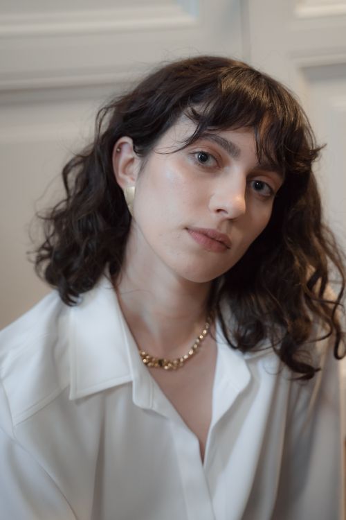 Free A thoughtful portrait of a woman with wavy hair wearing a white shirt and necklace. Stock Photo