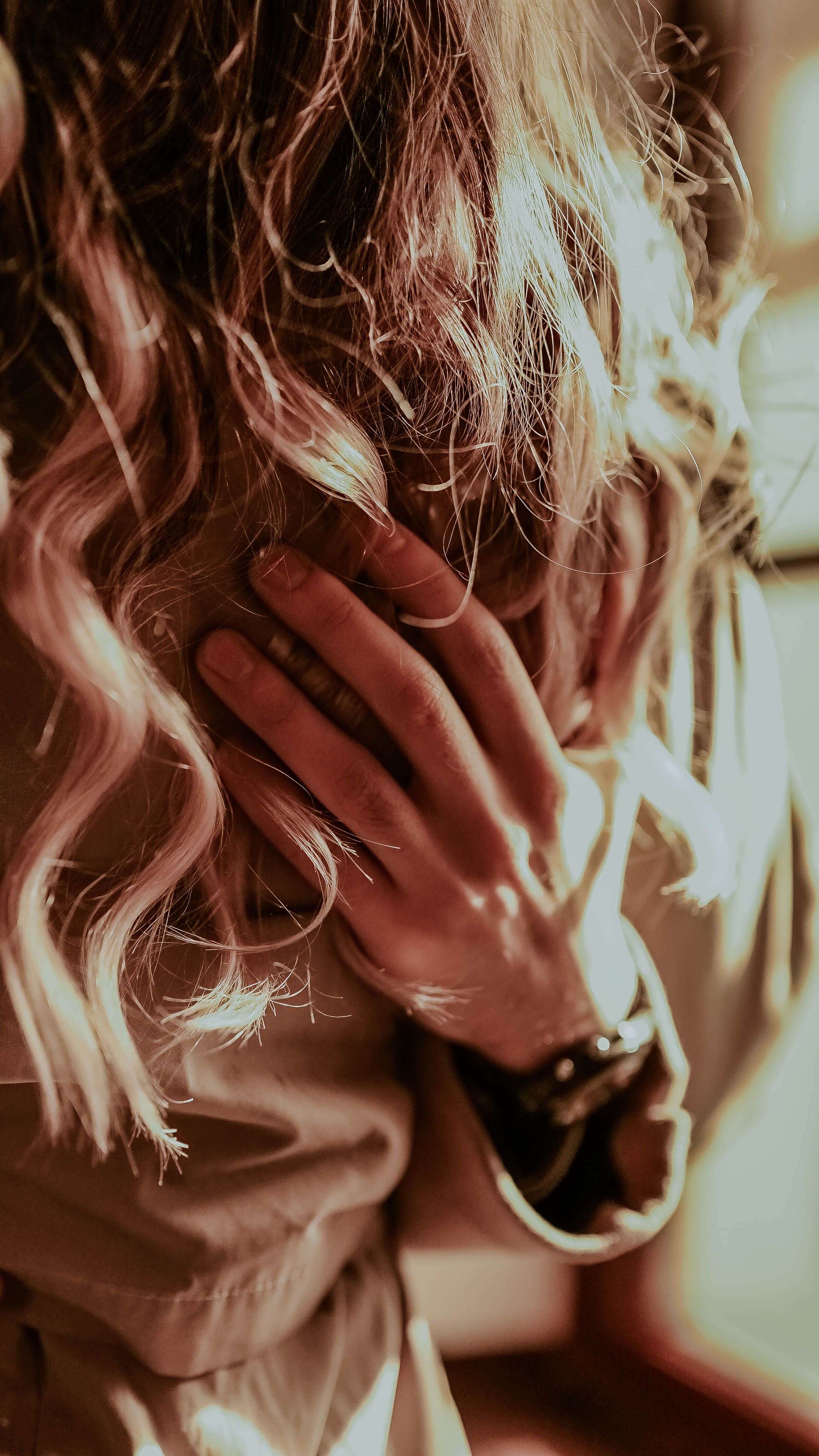 Artistic close-up of a woman’s hand and blonde curly hair, with warm tones.