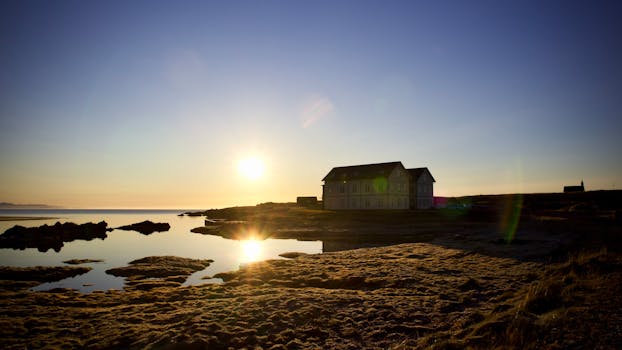 Breathtaking sunrise over the serene Icelandic coast, majestic building and calm sea reflecting the golden light.