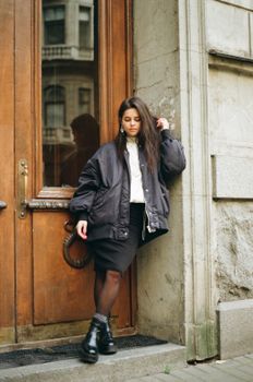 Teenage girl in stylish outfit leaning against a vintage door in an urban environment.
