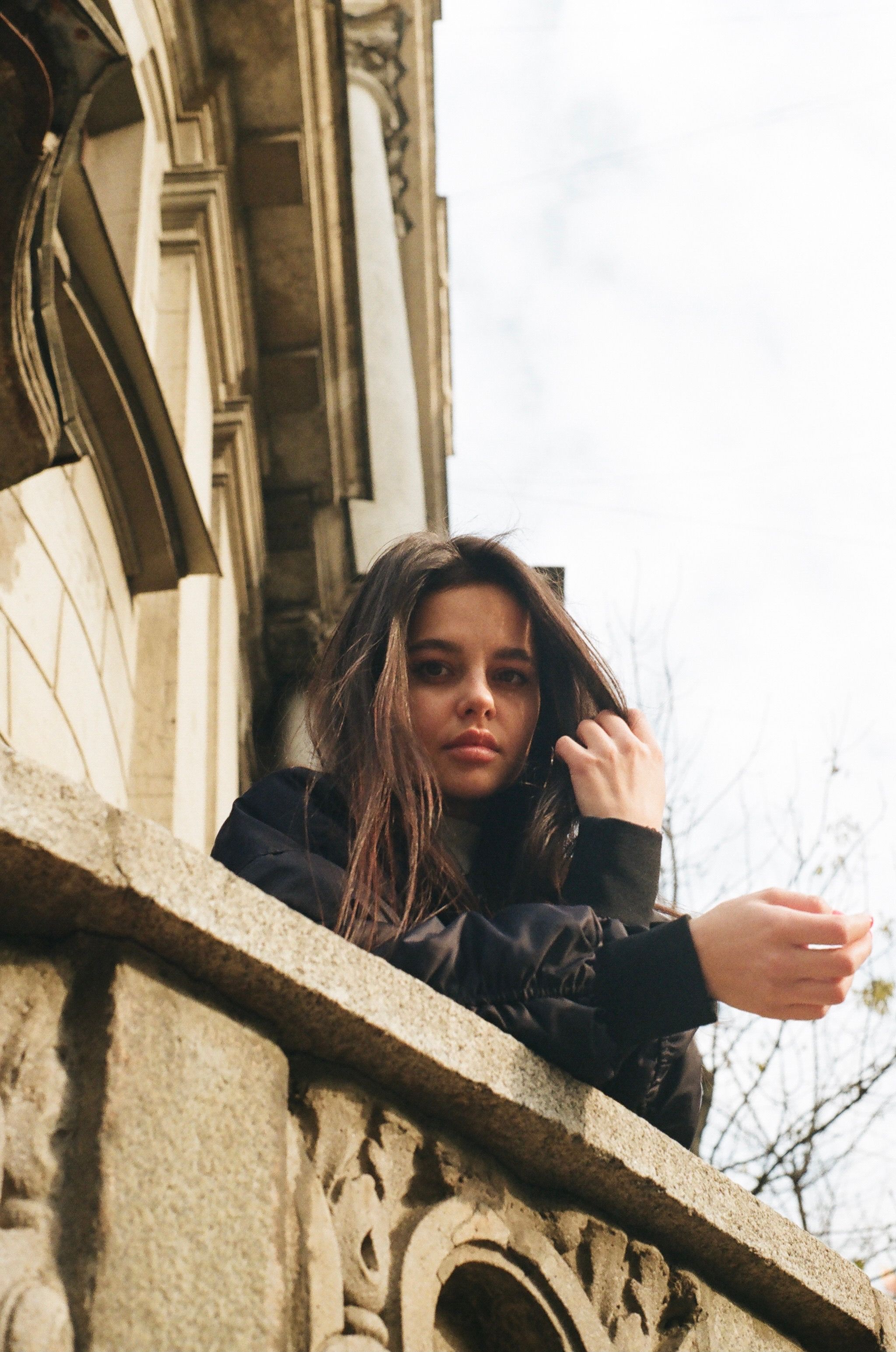 A woman leans on a decorative stone balustrade, with architectural details in the background.