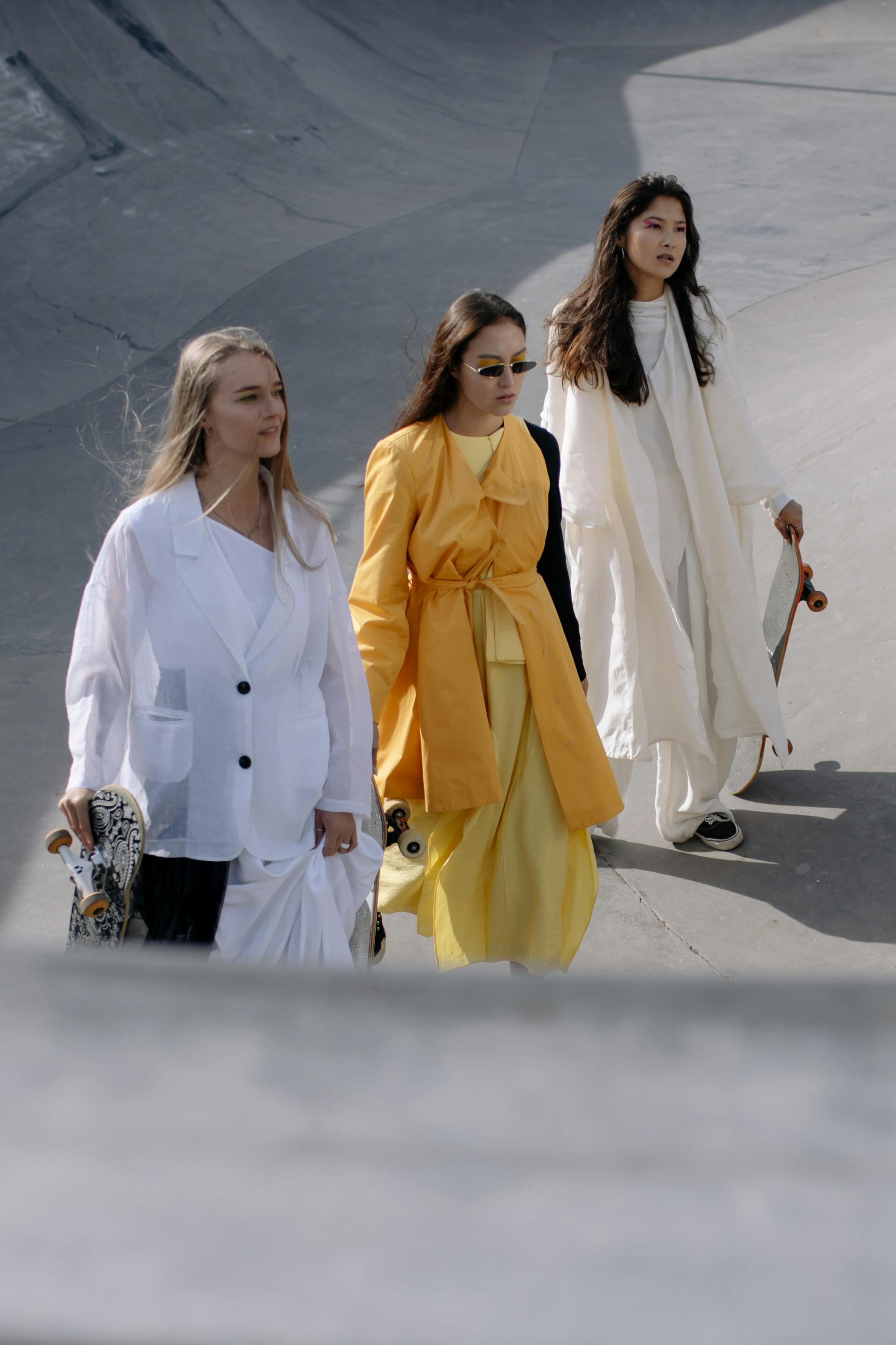 women in long dresses holding skateboard walking on skate park