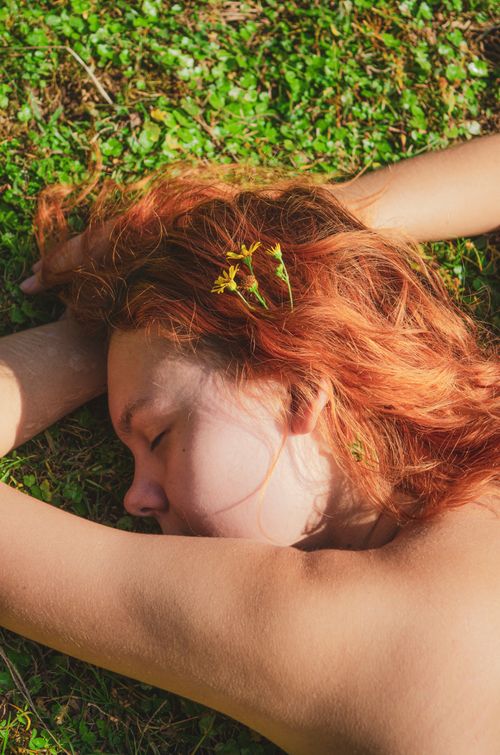 Free Shirtless woman with closed eyes and flowers in hair lying on grass. Stock Photo