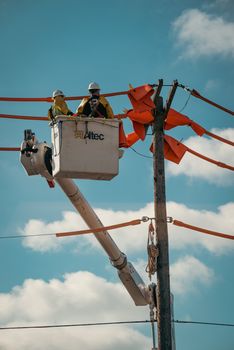 Two utility workers in a bucket truck repairing power lines on a sunny day.