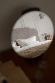 Cozy modern bedroom interior with a made bed reflected in a round mirror.