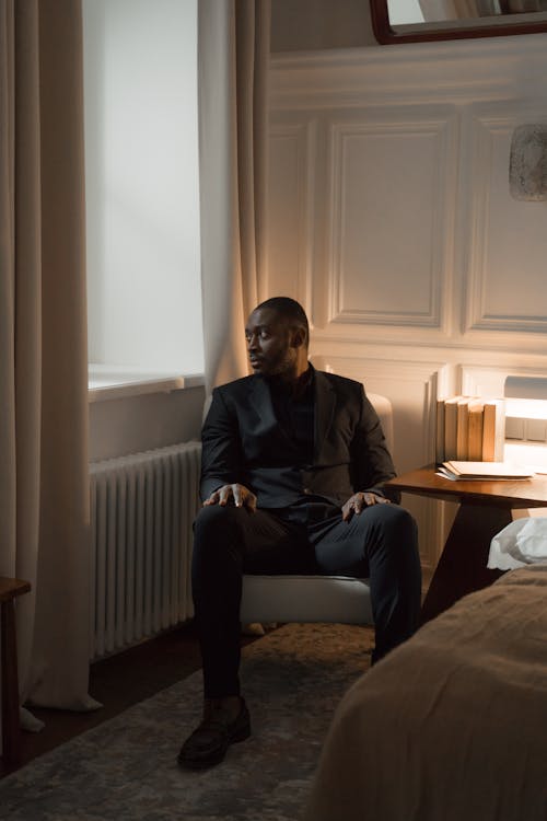 A Man in a Suit Sitting on a Chair while Looking Outside