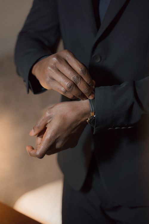 Free Close-up of an individual adjusting a wristwatch while wearing a black suit, exuding sophistication. Stock Photo