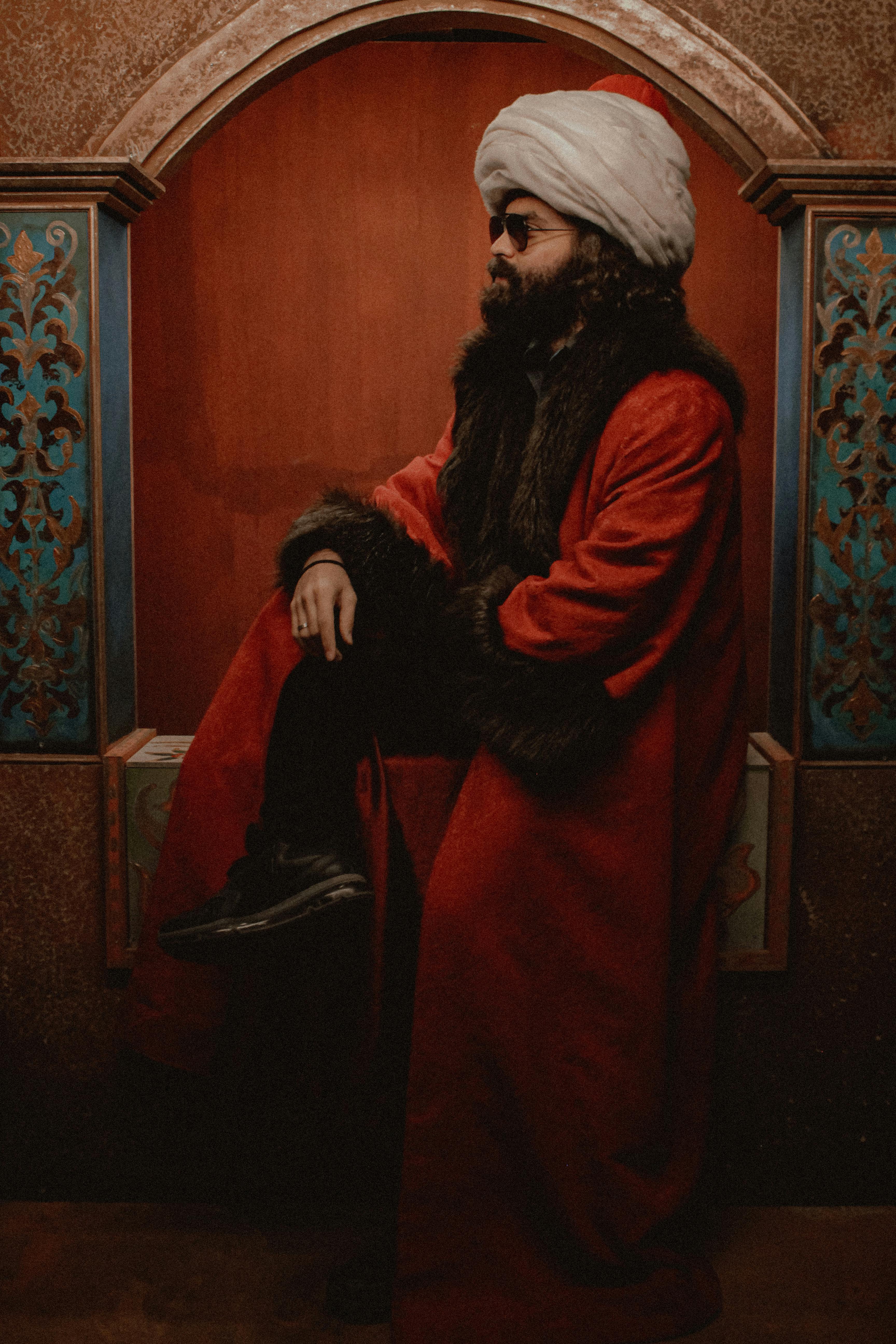 Portrait of a man in traditional Ottoman clothing and turban, set indoors with dim lighting.