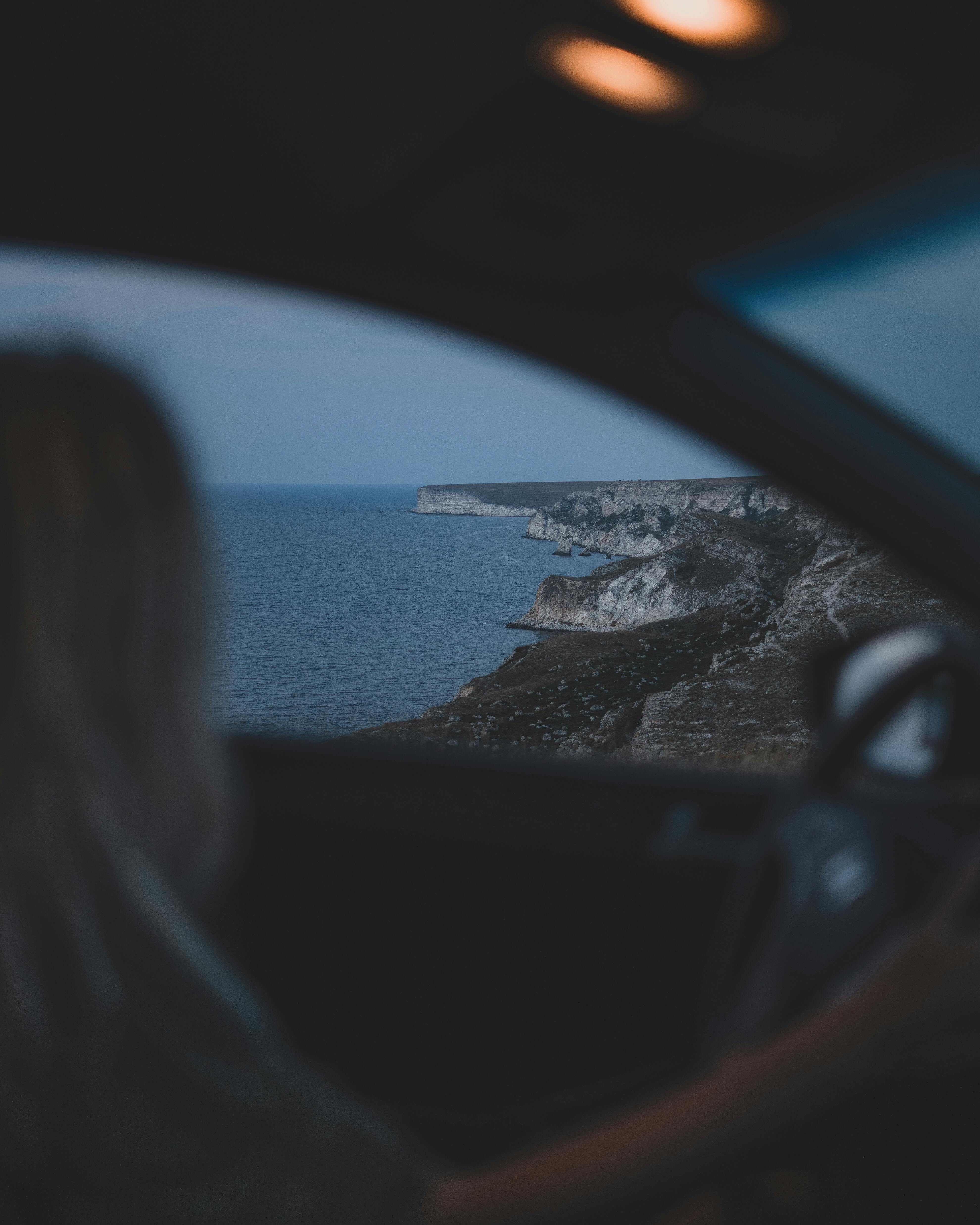 A person driving along a scenic coastal road at twilight, showing cliffs and ocean.
