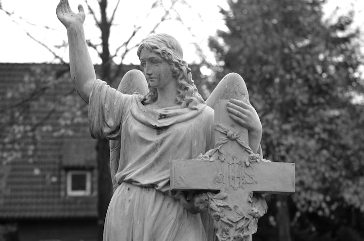 Grayscale Photo Of An Angel Statue And A Cross