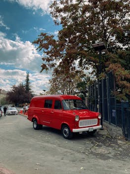 A vibrant red vintage van parked on a leafy street under a clear sky.
