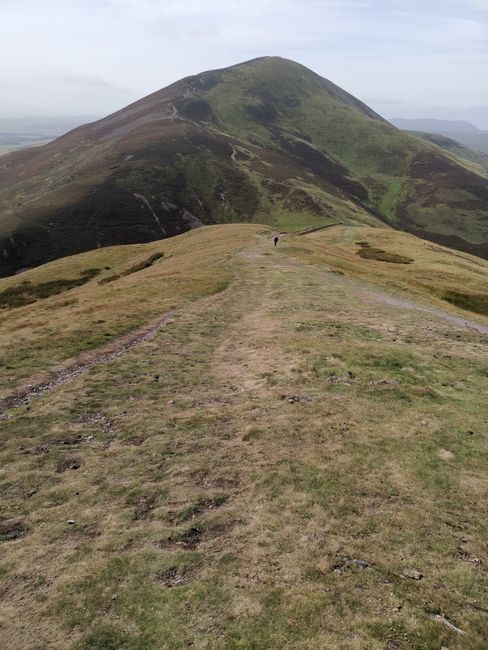 A scenic hiking trail leading to rolling hills under a clear sky in the UK countryside.
