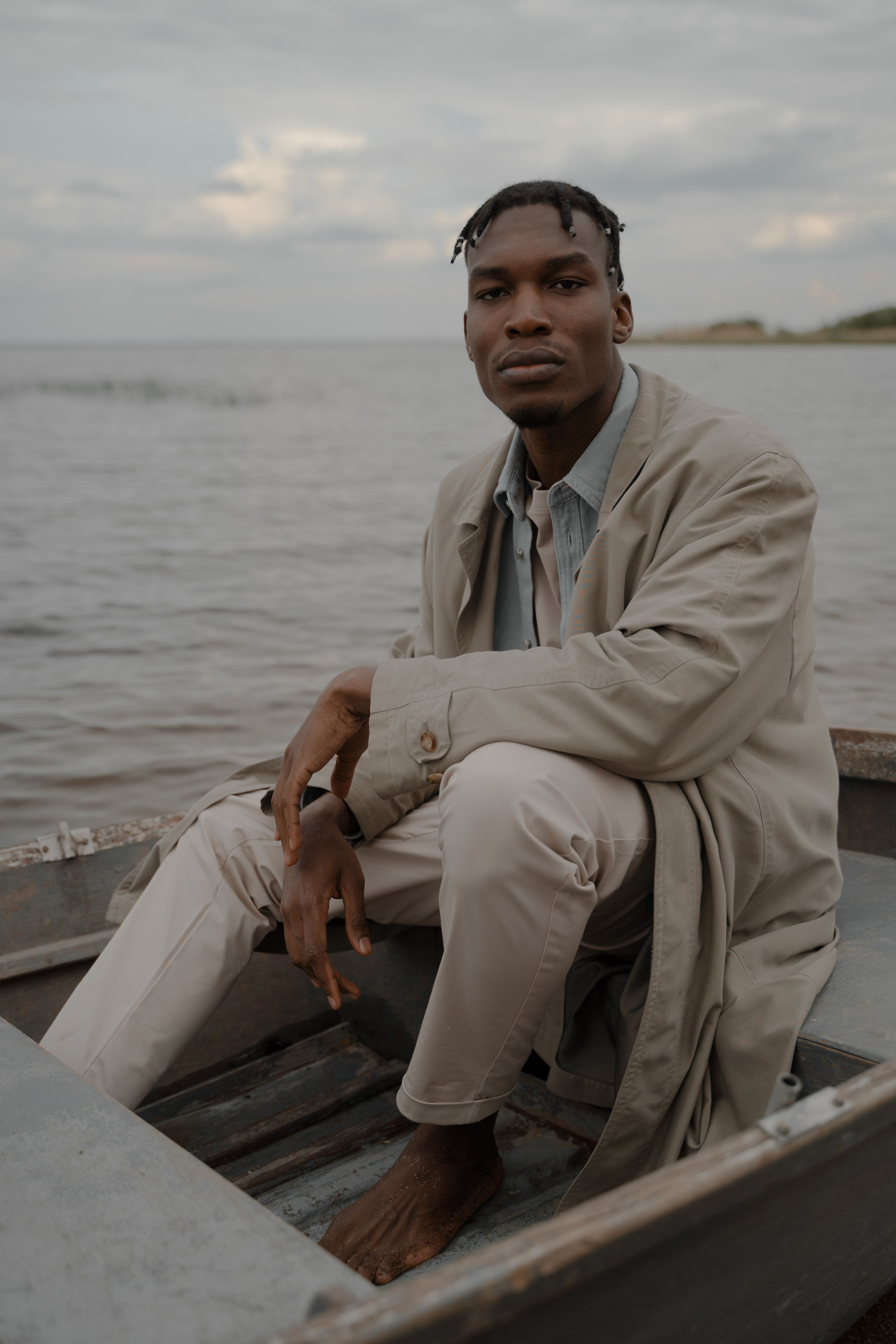 Young man with braided hair sitting barefoot on a boat by the sea.