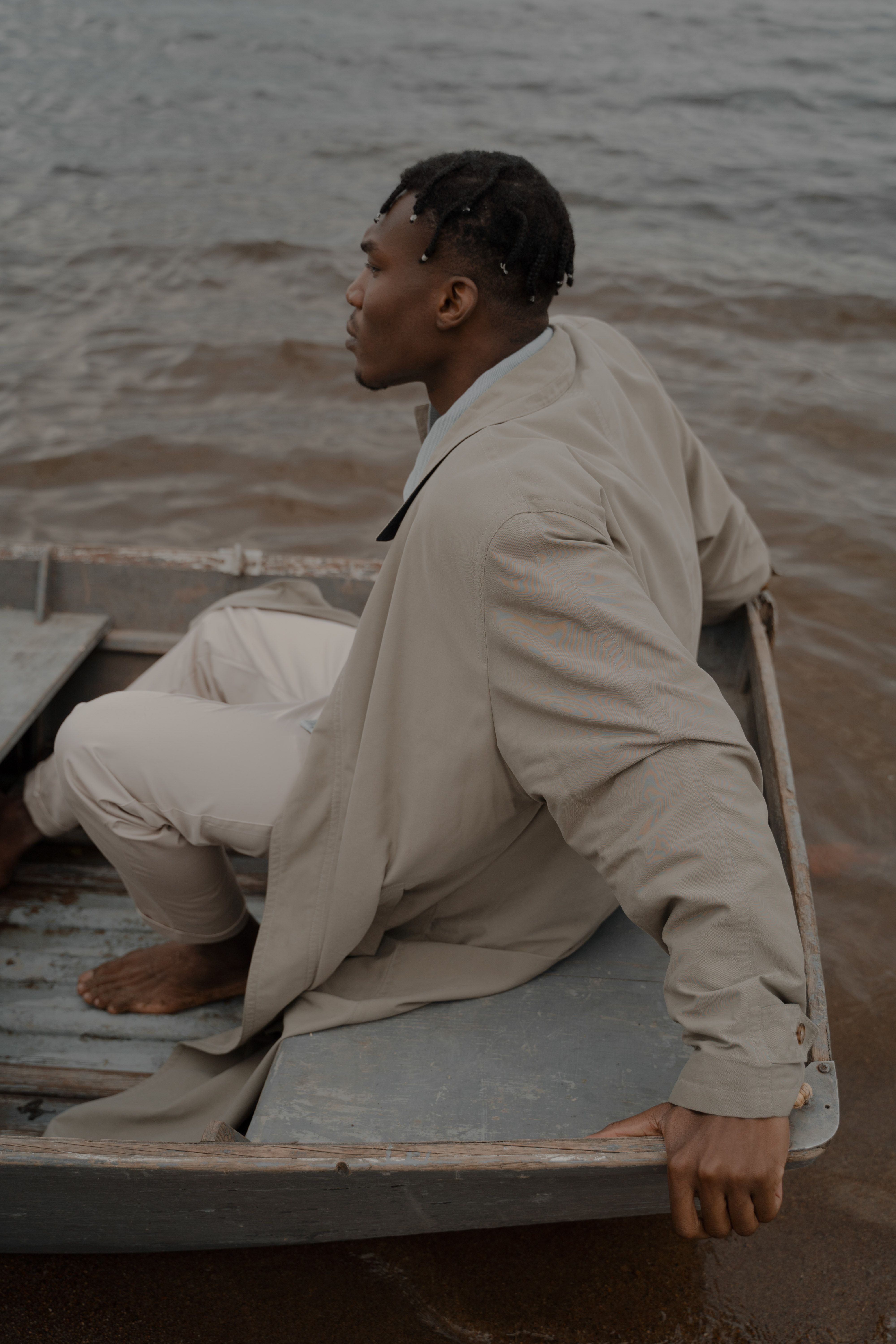 A man sits barefoot in a boat on a serene beach shore, gazing out over the water.