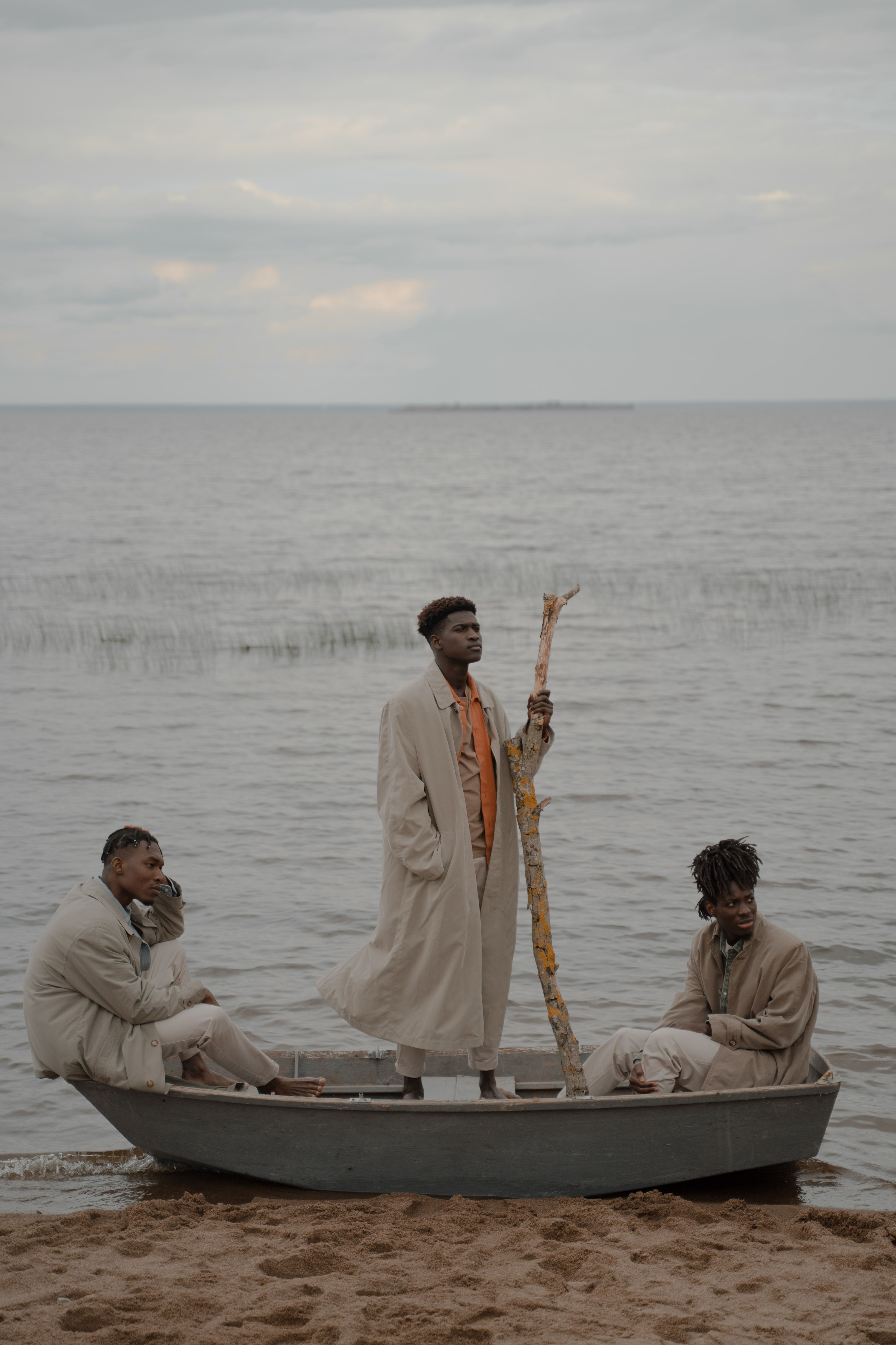Three men in a boat on a serene beach, wearing trench coats and capturing a moment of tranquility.