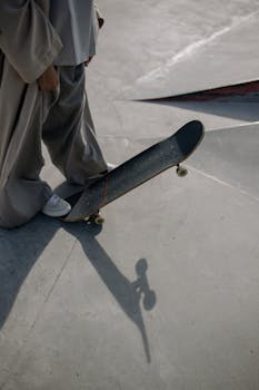 A person stands with a skateboard in a concrete skate park, casting a shadow on the ground.