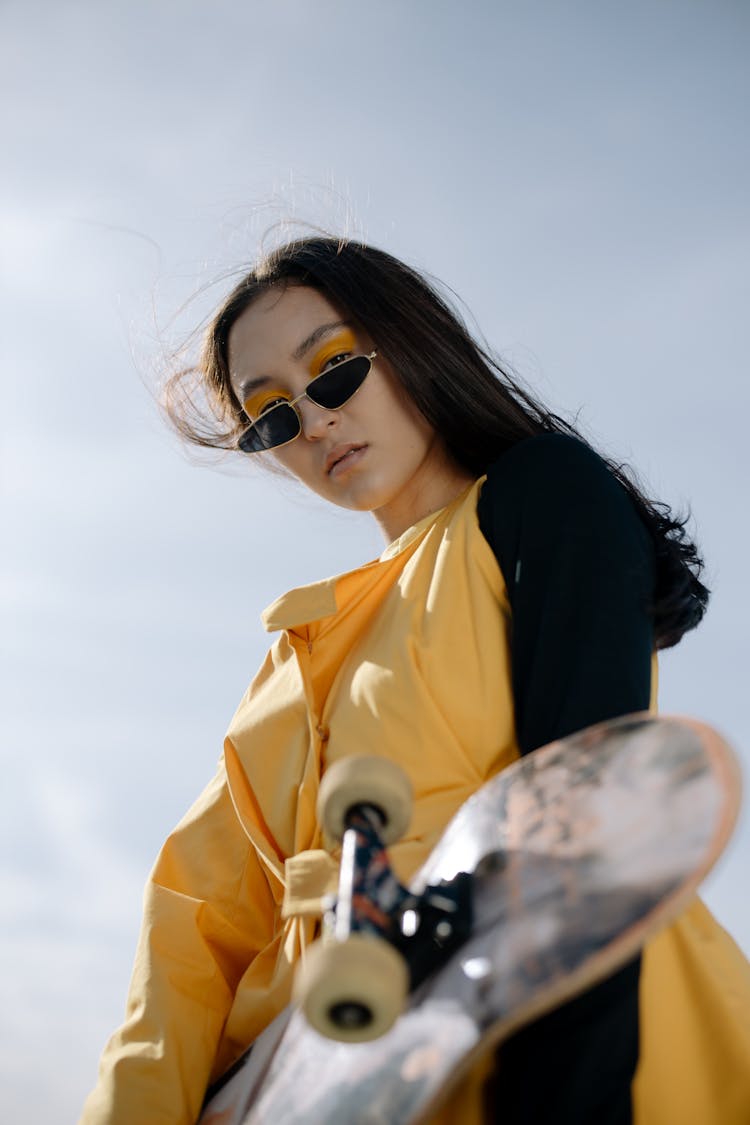 A Woman In Yellow Dress With Black Log Sleeves Holding A Skateboard