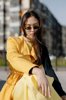 Elegant woman in fashionable yellow coat and dress posing outdoors with sunglasses.