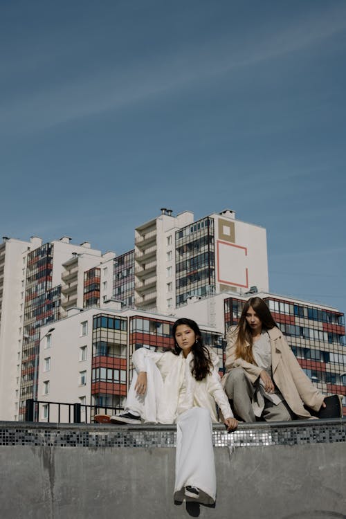 Women Sitting on a Concrete Fence Near Tall Buildings