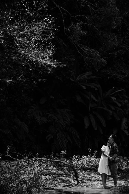 A couple lovingly embraces in a lush, shaded forest captured in black and white.