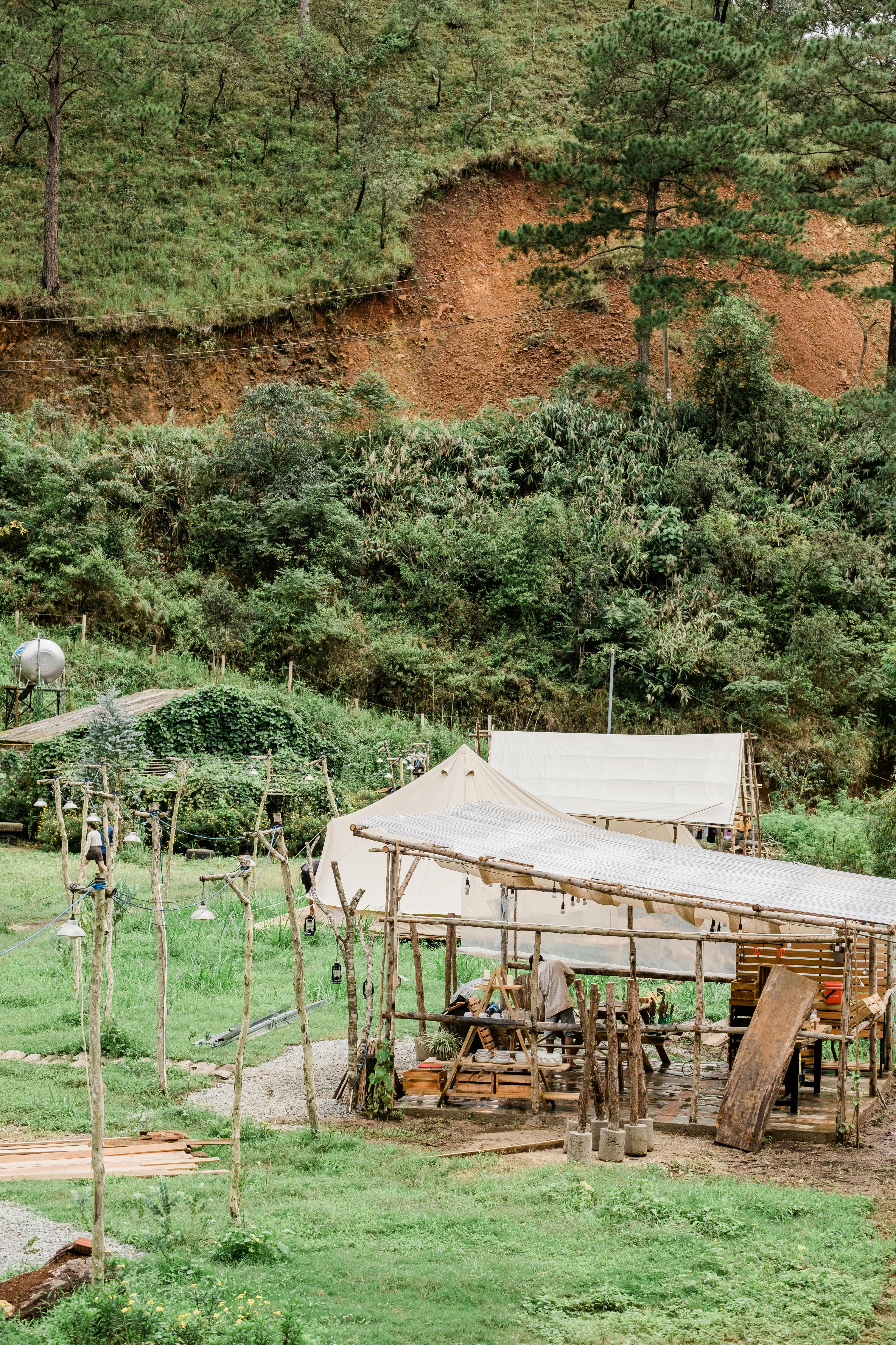 A rural area with wooden shelters set against a lush green hillside landscape.